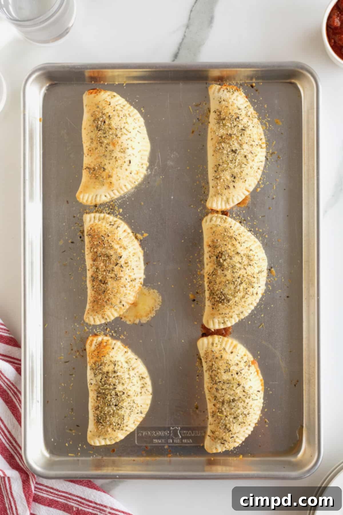 Six crescent shaped mini calzones on an aluminum baking sheet.