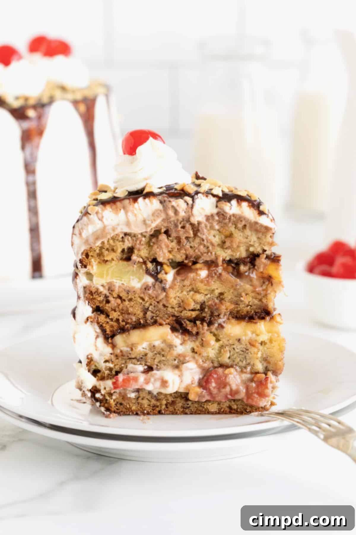Banana Split Dream Cake 2 A vibrant slice of Banana Split Cake on a pristine white dessert plate, with a fork gently resting beside it. The cake reveals beautifully layered textures.