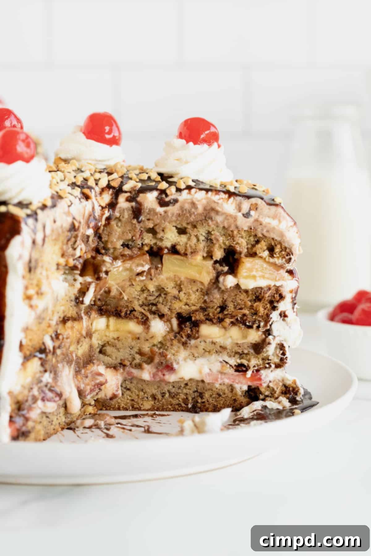 Banana Split Dream Cake 11 A beautifully presented Banana Split Cake on a white cake plate, with a portion sliced out, revealing its enticing layers.