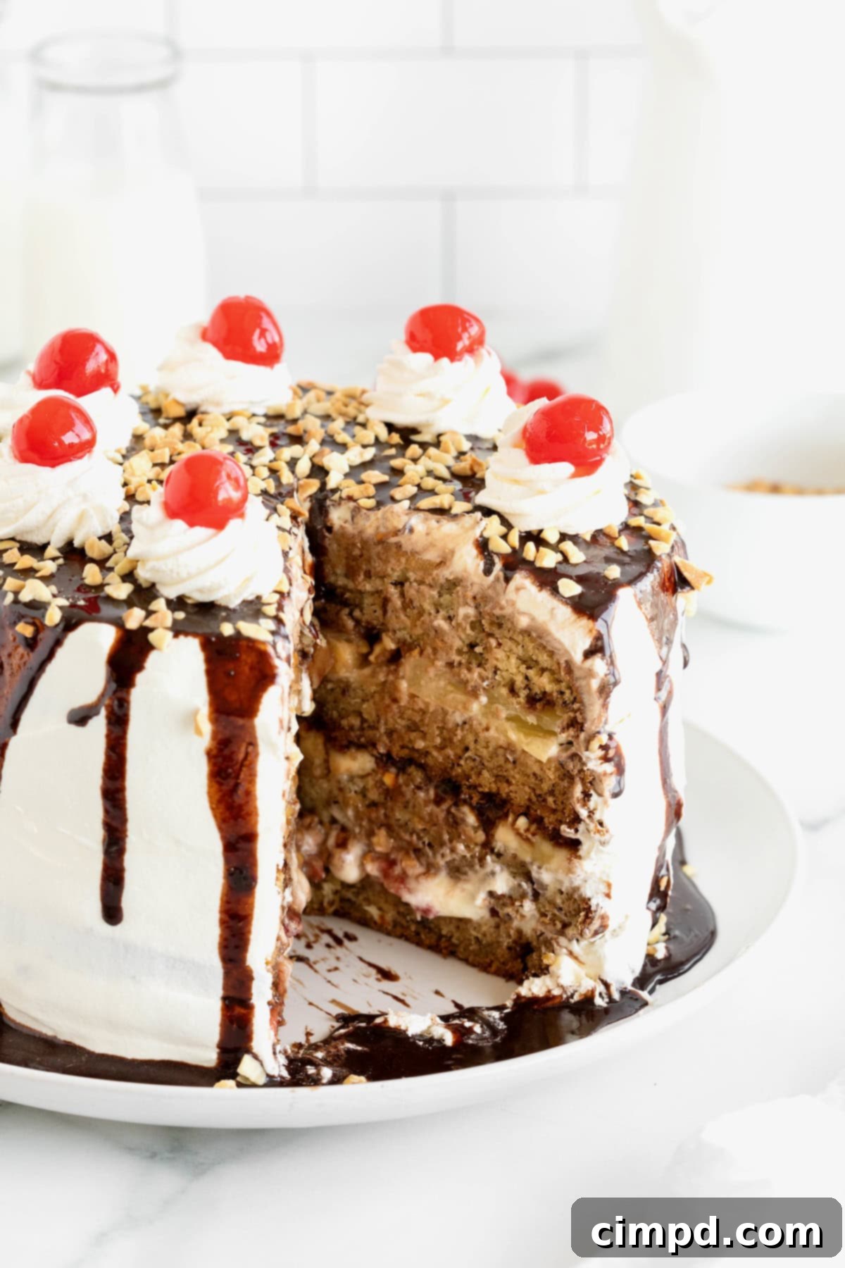 Banana Split Dream Cake 4 A delectable Banana Split Cake displayed on a white cake plate, showcasing a generous slice removed to reveal its three magnificent layers.