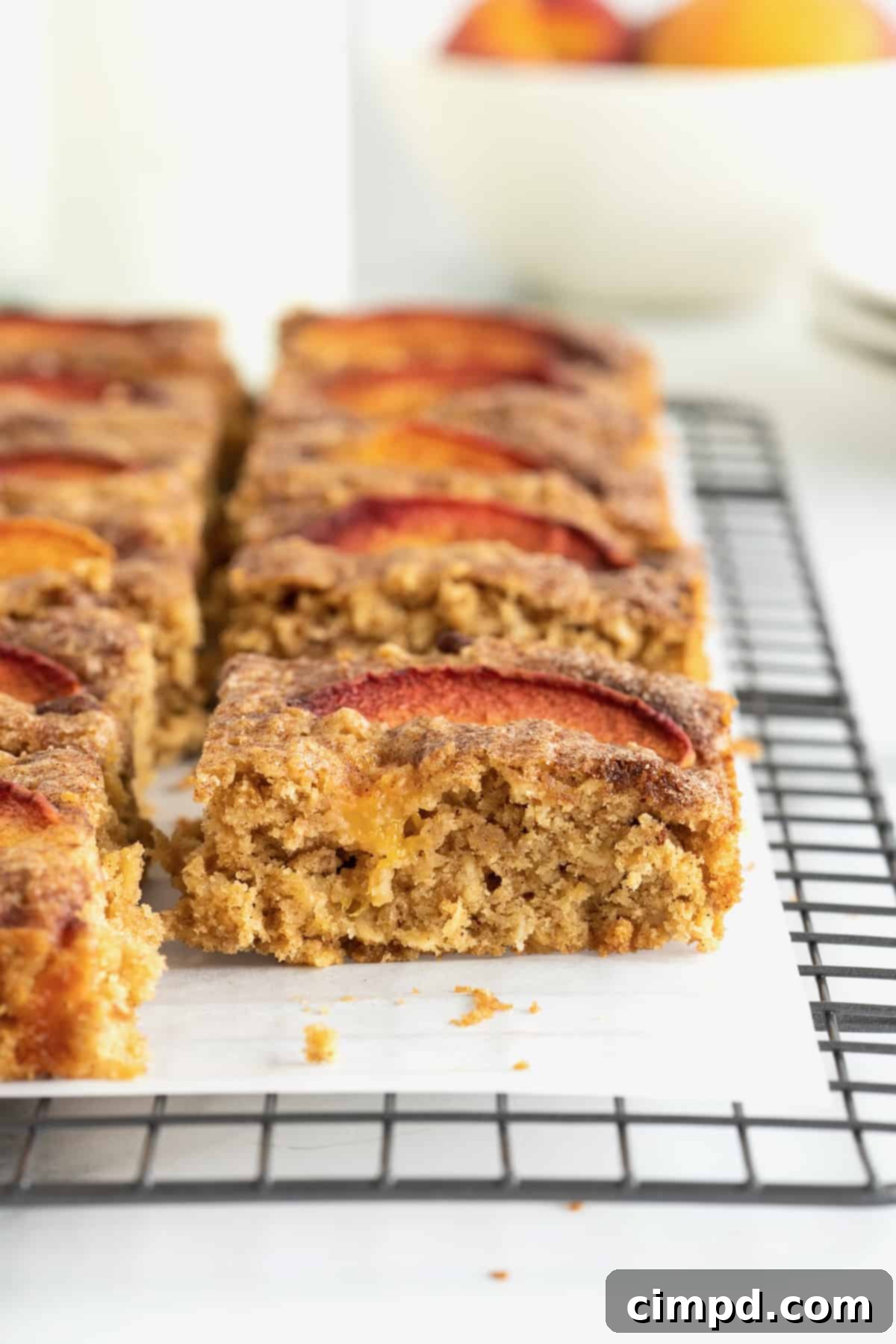 Golden brown oatmeal bars with fresh peach slices on top, cooling on a parchment-lined rack.