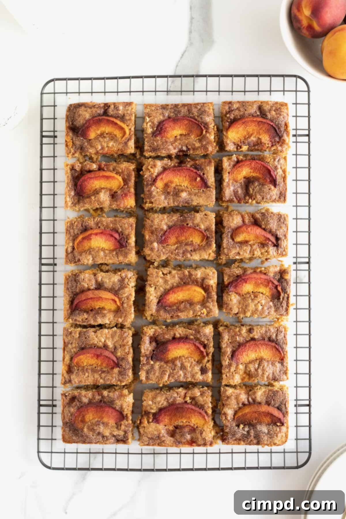 A cooling rack covered in parchment paper holds eighteen neatly cut squares of Peach Oatmeal Bars.