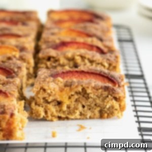 Golden brown oatmeal bars with fresh peach slices on top, cooling on a parchment-lined rack.