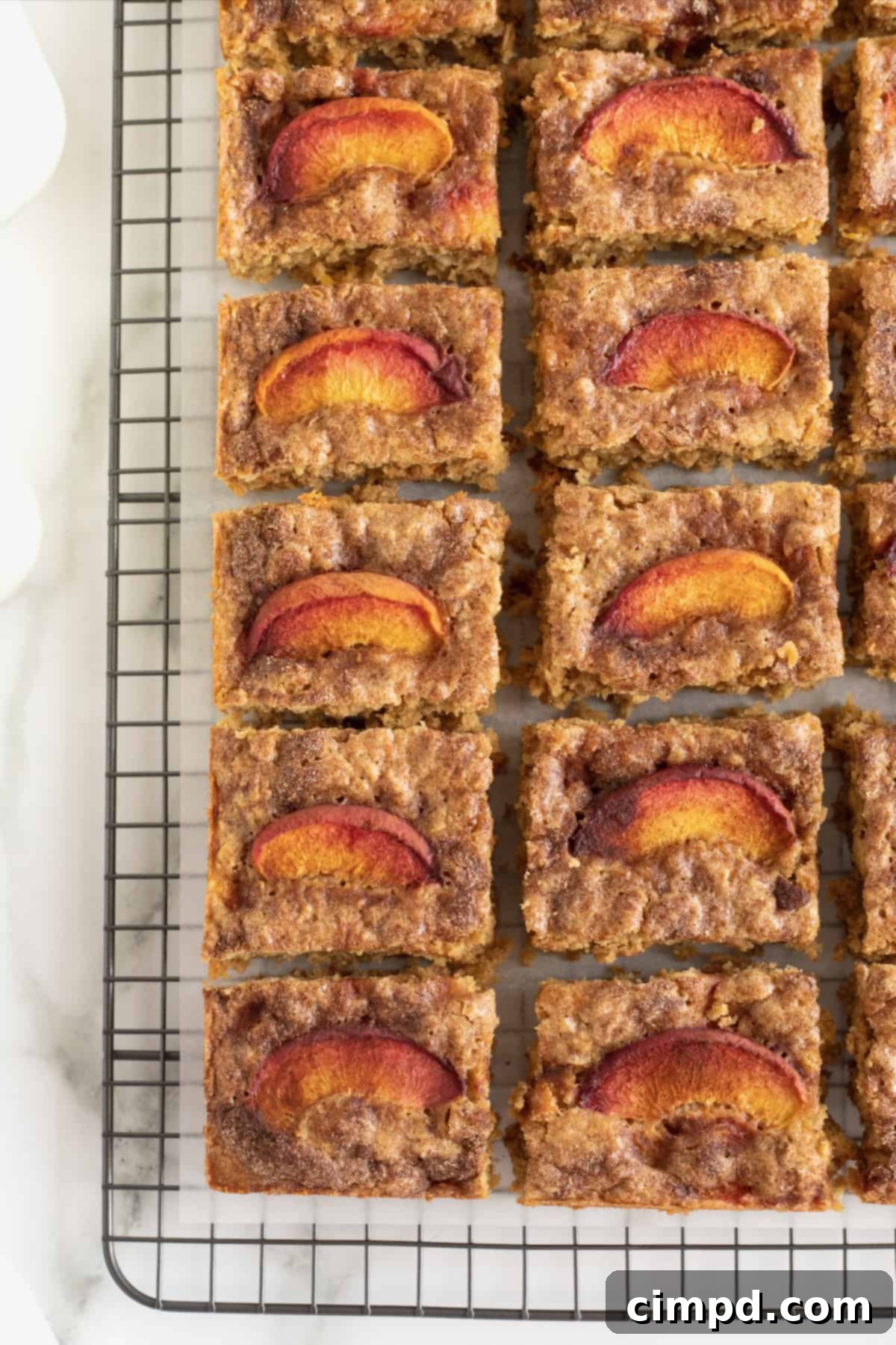 Eighteen perfectly cut squares of Peach Oatmeal Bars arranged on a cooling rack covered with parchment paper.