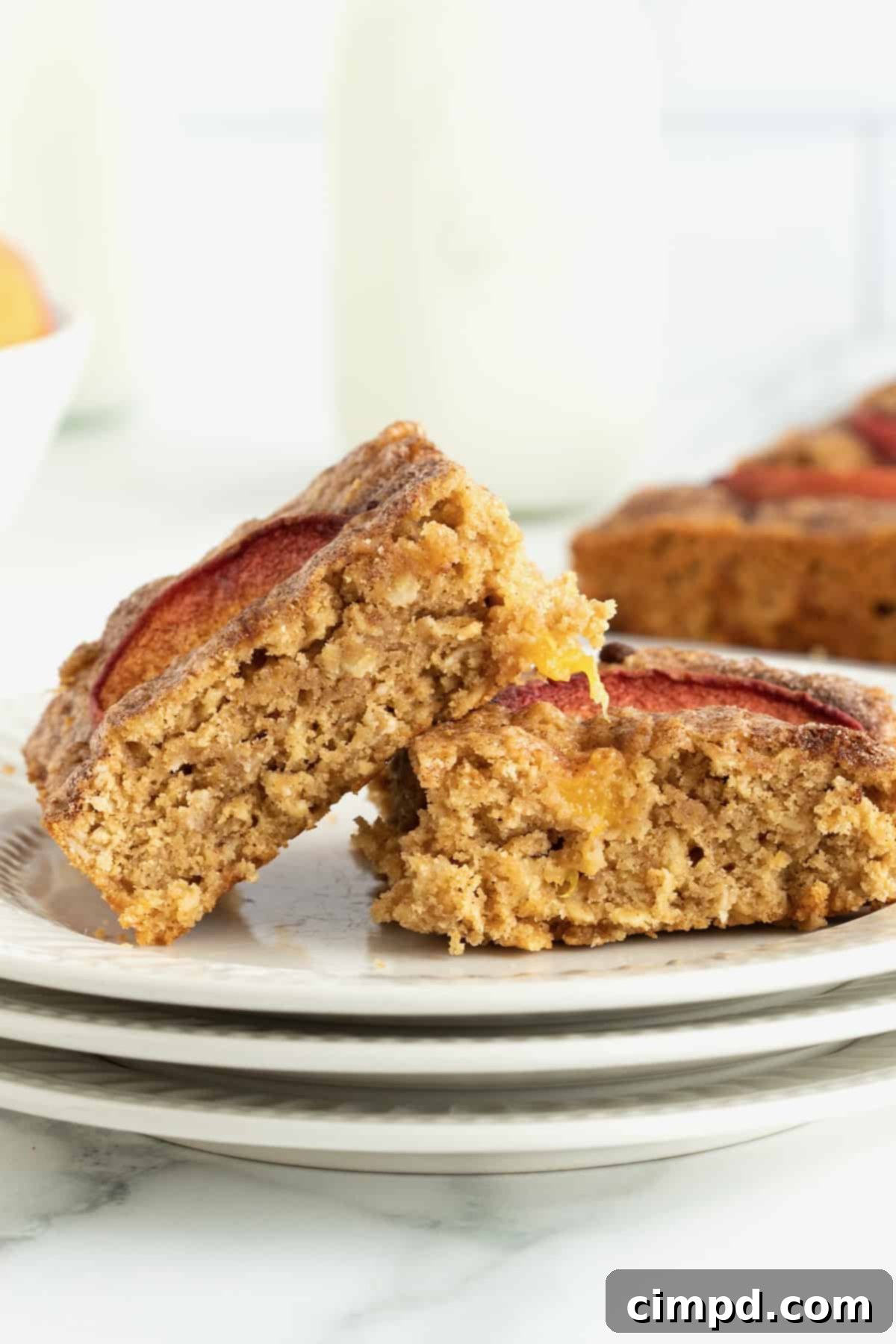 Two enticing peach oatmeal snack bars, garnished with fresh peach slices, presented on a pristine white plate.