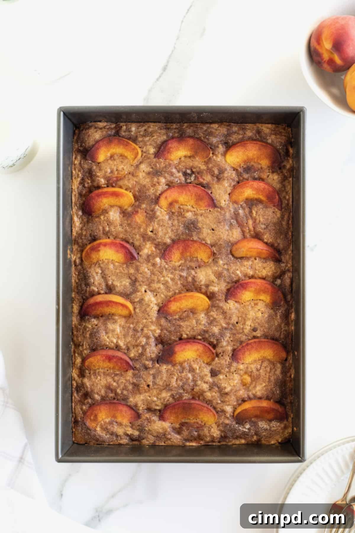 A 9x13 inch pan filled with freshly baked oatmeal bars, beautifully topped with vibrant fresh peach slices.