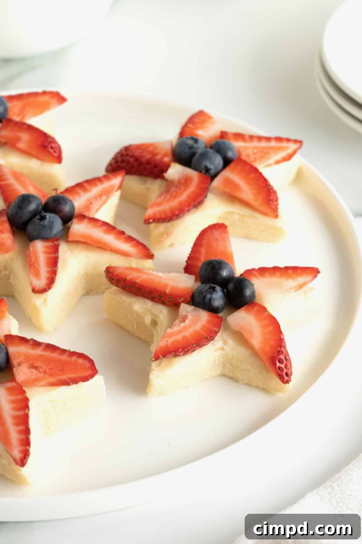 Star-Spangled Celebration Cookies 5 A festive display of star shaped shortbread cookies with strawberry slices and blueberries, presented on a round, white platter, perfect for a patriotic gathering.