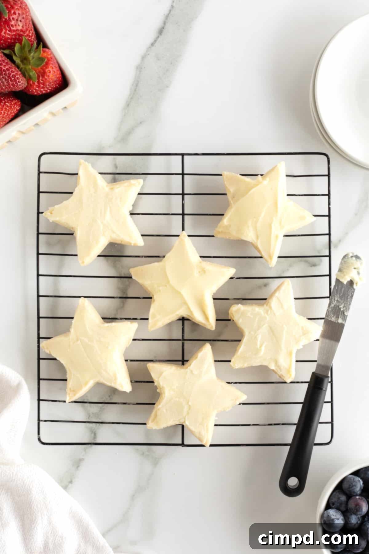 Star-Spangled Celebration Cookies 9 Star shaped shortbread cookies meticulously covered with a smooth, white cream cheese frosting, ready for the fruit topping.