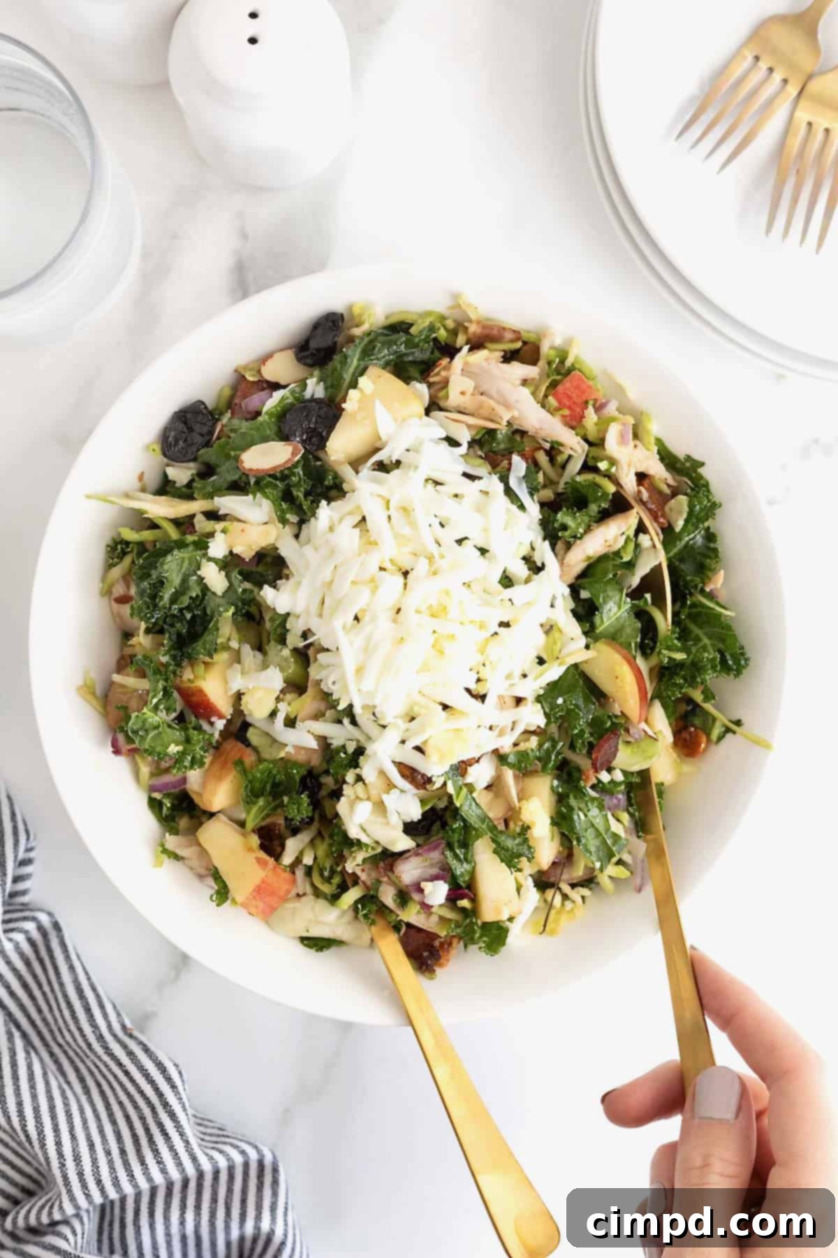 A kale and roasted chicken salad with chopped pecans in a large white serving bowl. 