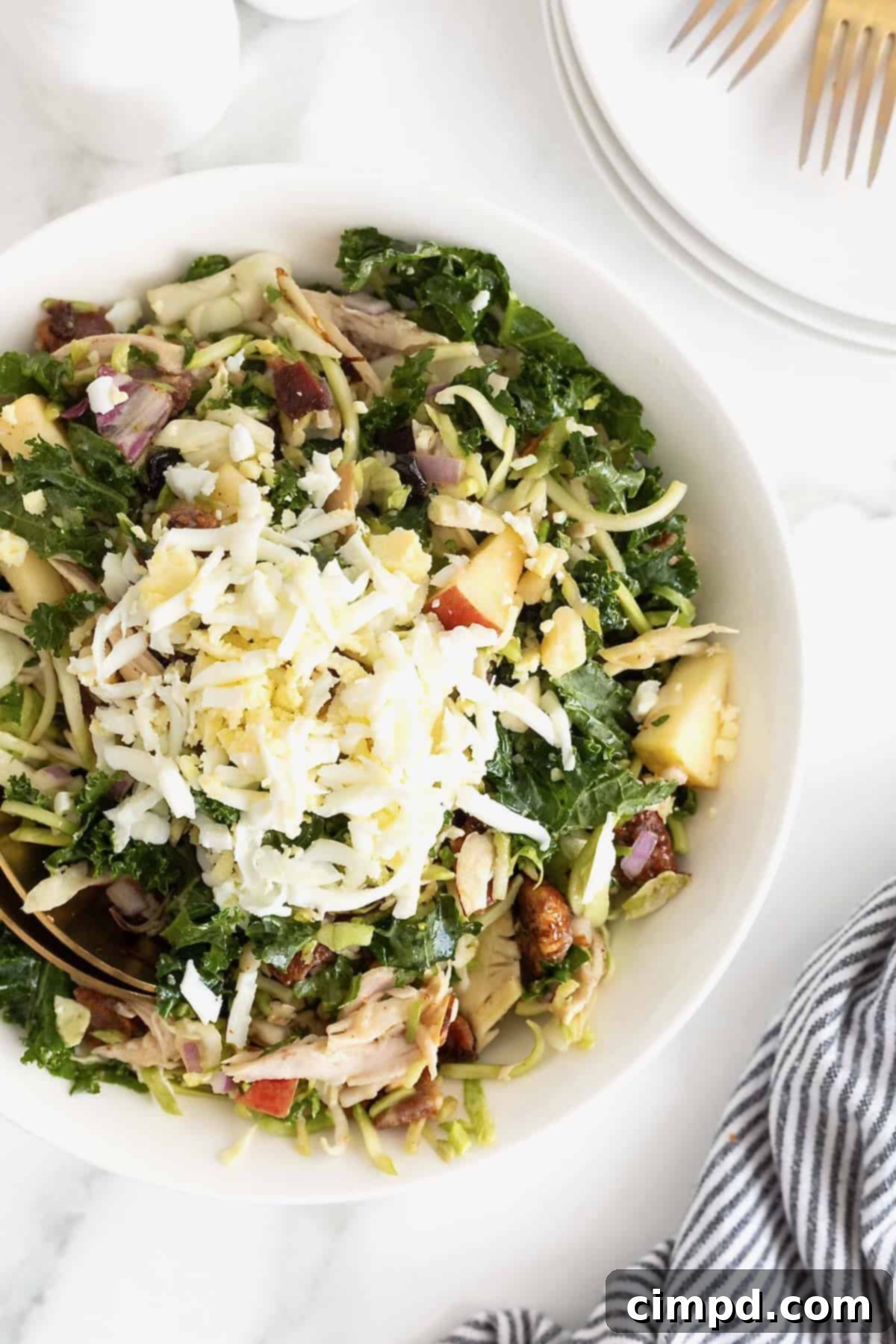 A kale and roasted chicken salad with chopped pecans in a large white serving bowl.
