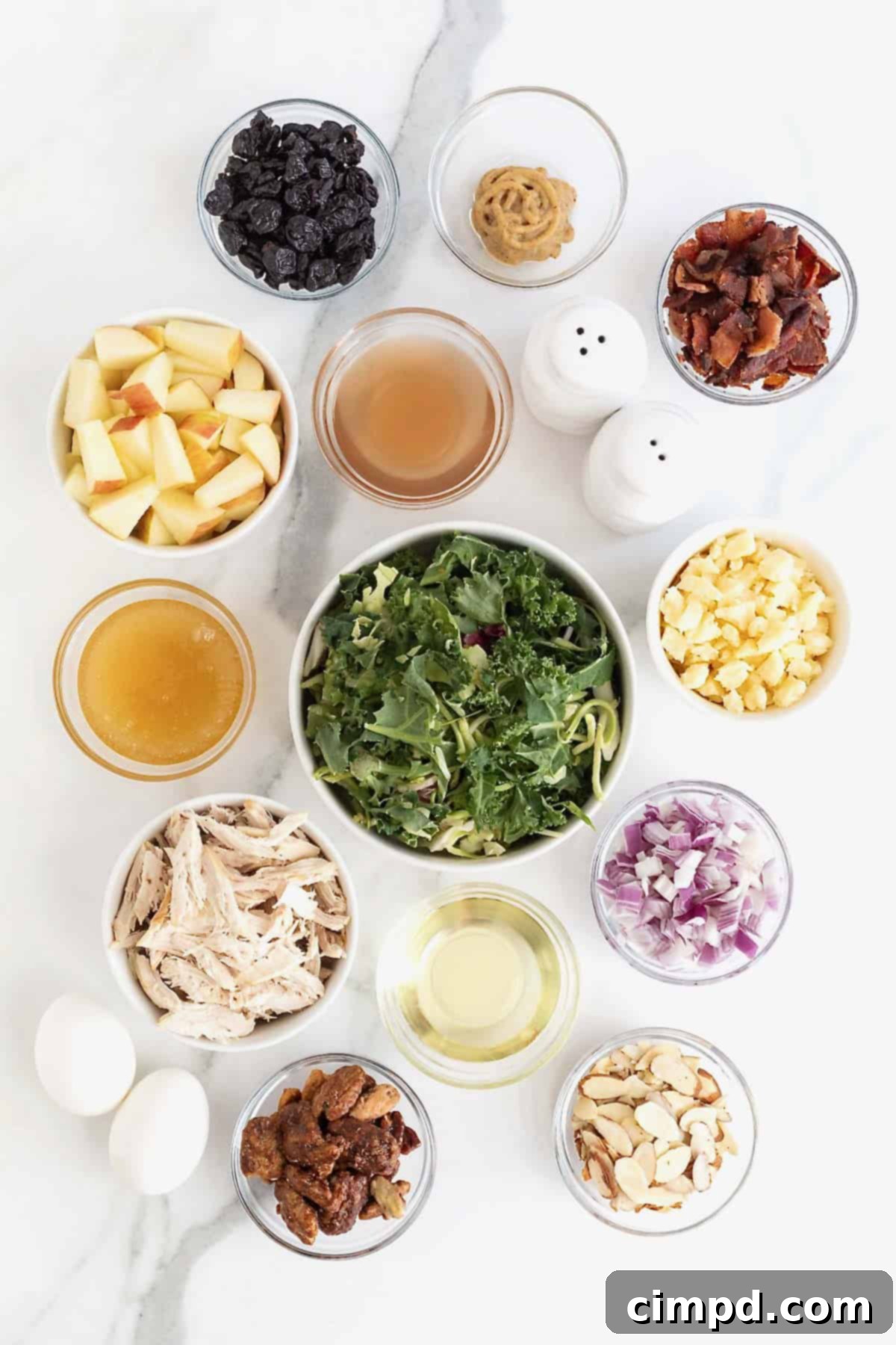 Ingredients to make a kale and roasted chicken salad in small glass dishes on a white marble counter.