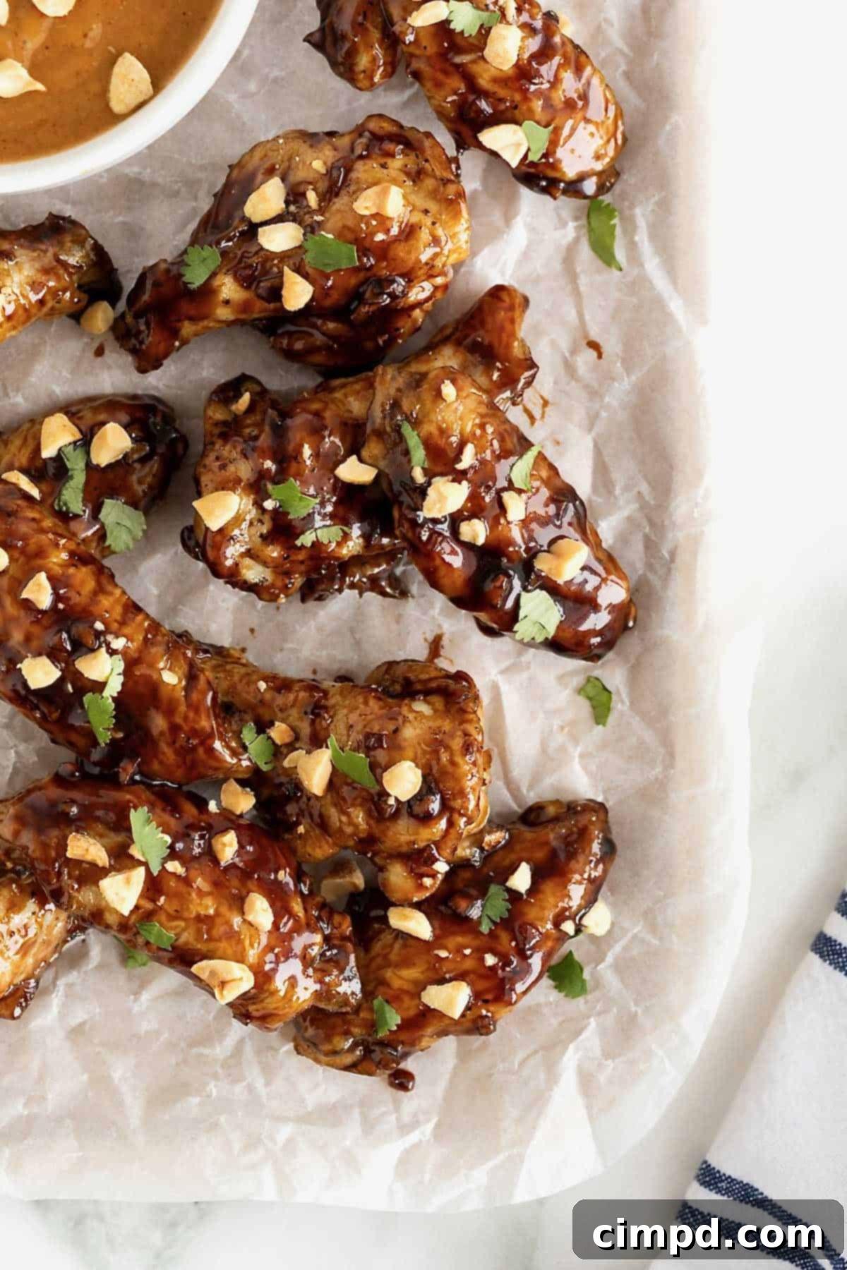 A close-up shot of Baked Crispy Asian Chicken Wings, artfully arranged and garnished with vibrant green cilantro and crunchy crushed peanuts on a clean white surface.