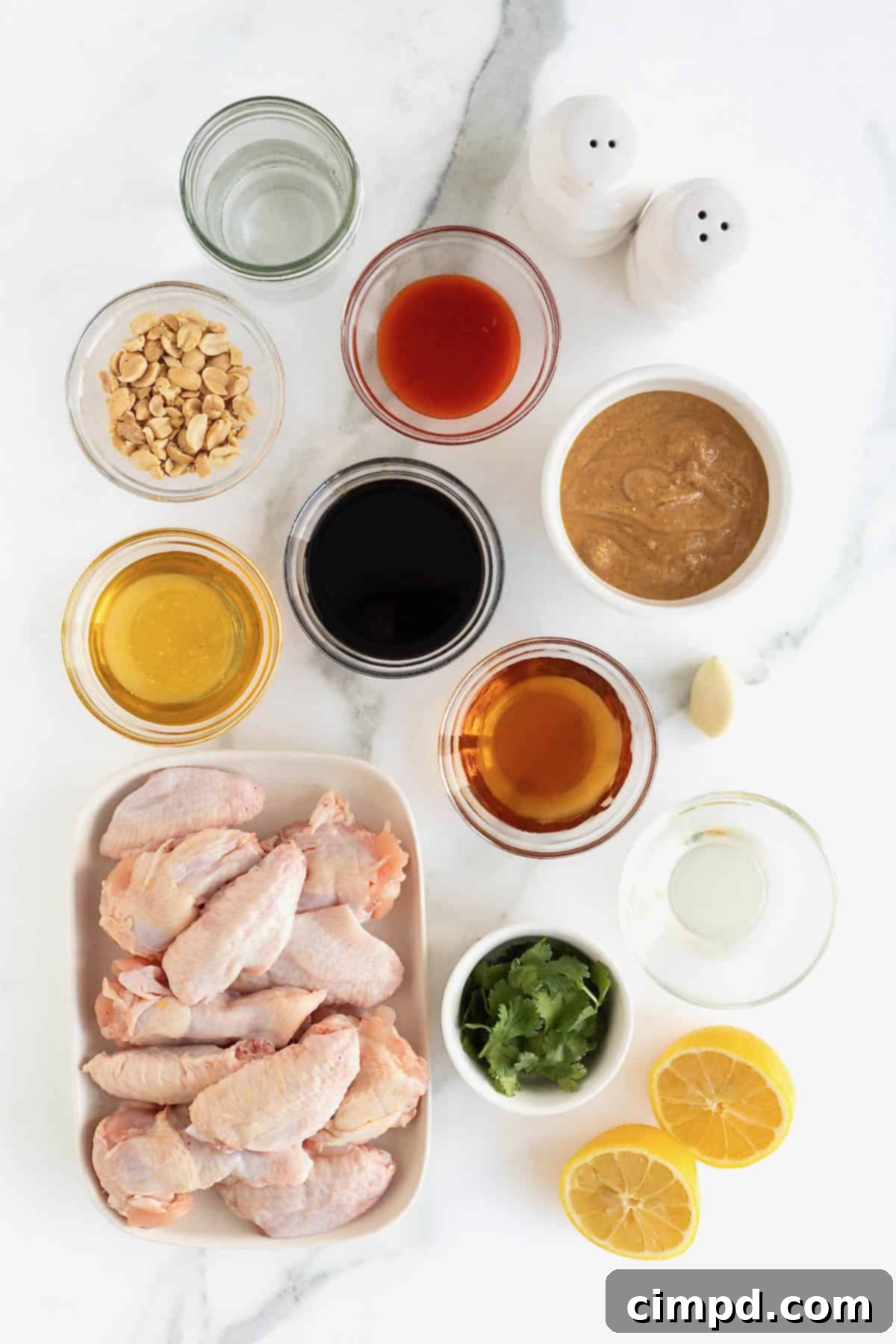 An array of fresh ingredients for Baked Crispy Asian Chicken Wings, neatly arranged in small glass bowls on a white marble countertop.