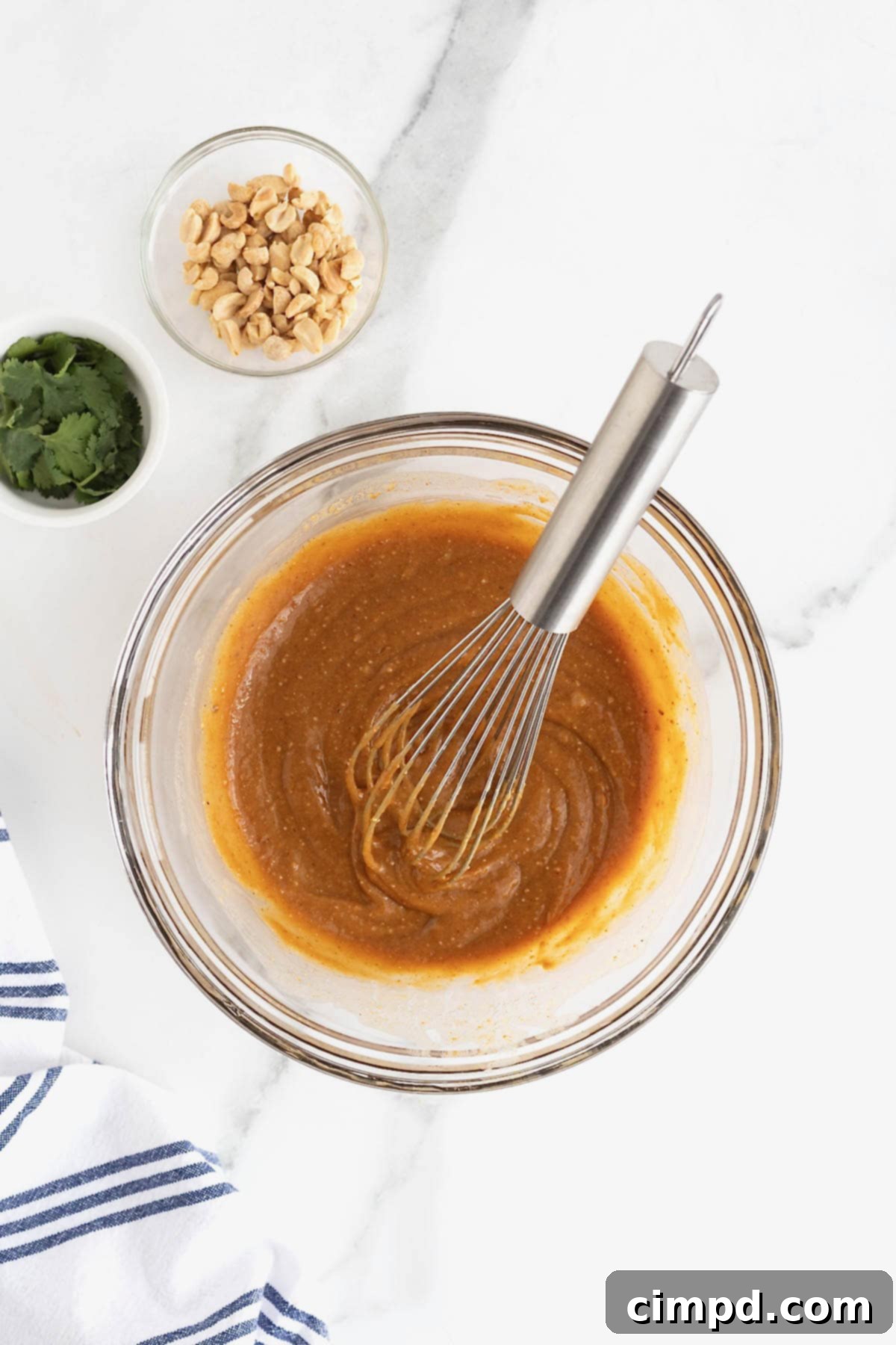 A glass bowl filled with rich, creamy peanut dipping sauce, with a whisk resting inside, ready for serving.
