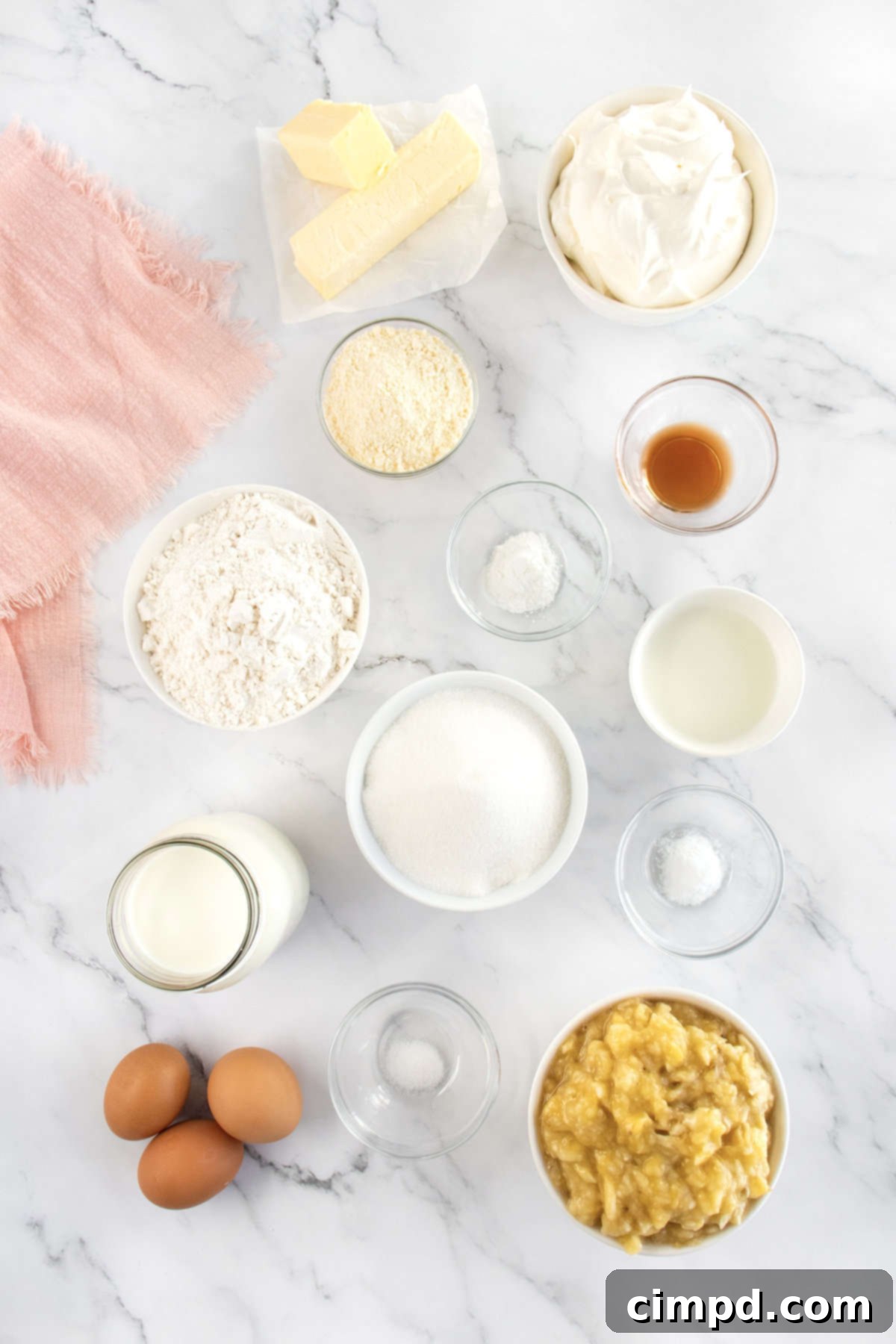 Ingredients for Banana Pudding Cupcakes laid out in small glass containers on a pristine white marble counter, ready for baking.