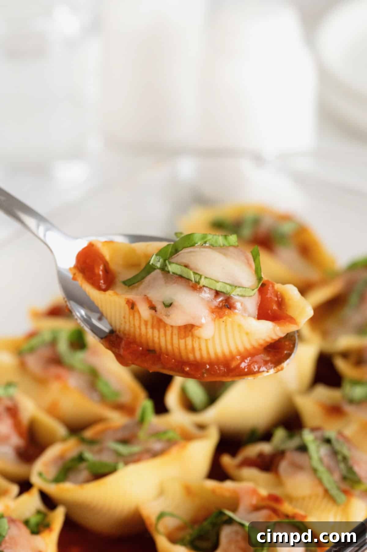 A metal serving spoon scooping out a meatball stuffed pasta shell.