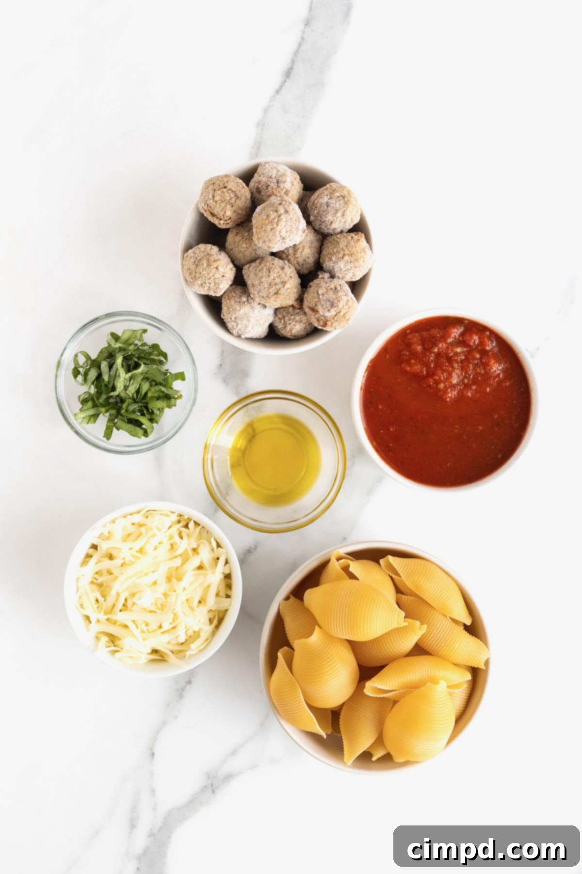 Ingredients to make meatballs stuffed shells in glass dishes on a white marble counter.