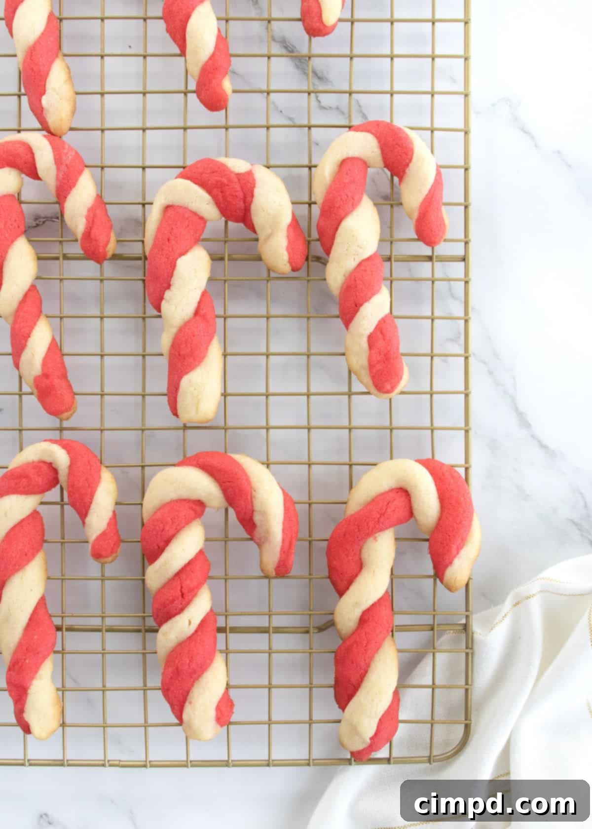 Six red and white sugar cookies shaped like candy canes on a brass cooling rack, ready to be enjoyed.
