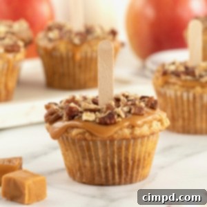 Gourmet Caramel Apple Cupcakes 12 A caramel apple cupcake, perfectly frosted with golden caramel and sprinkled with pecan pieces, featuring a whimsical popsicle stick in its center.