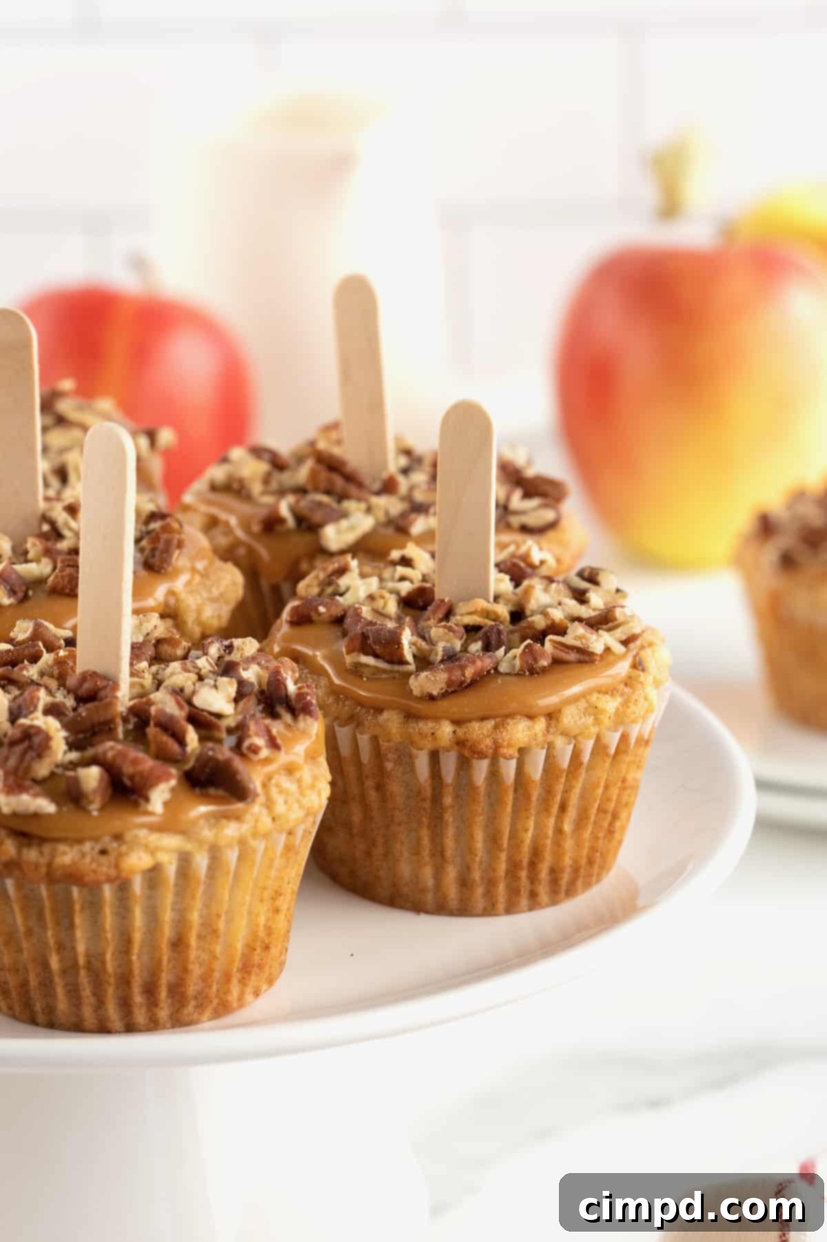 Gourmet Caramel Apple Cupcakes 4 A trio of caramel apple cupcakes, each adorned with creamy caramel, chopped pecans, and a fun popsicle stick, arranged artfully for presentation.
