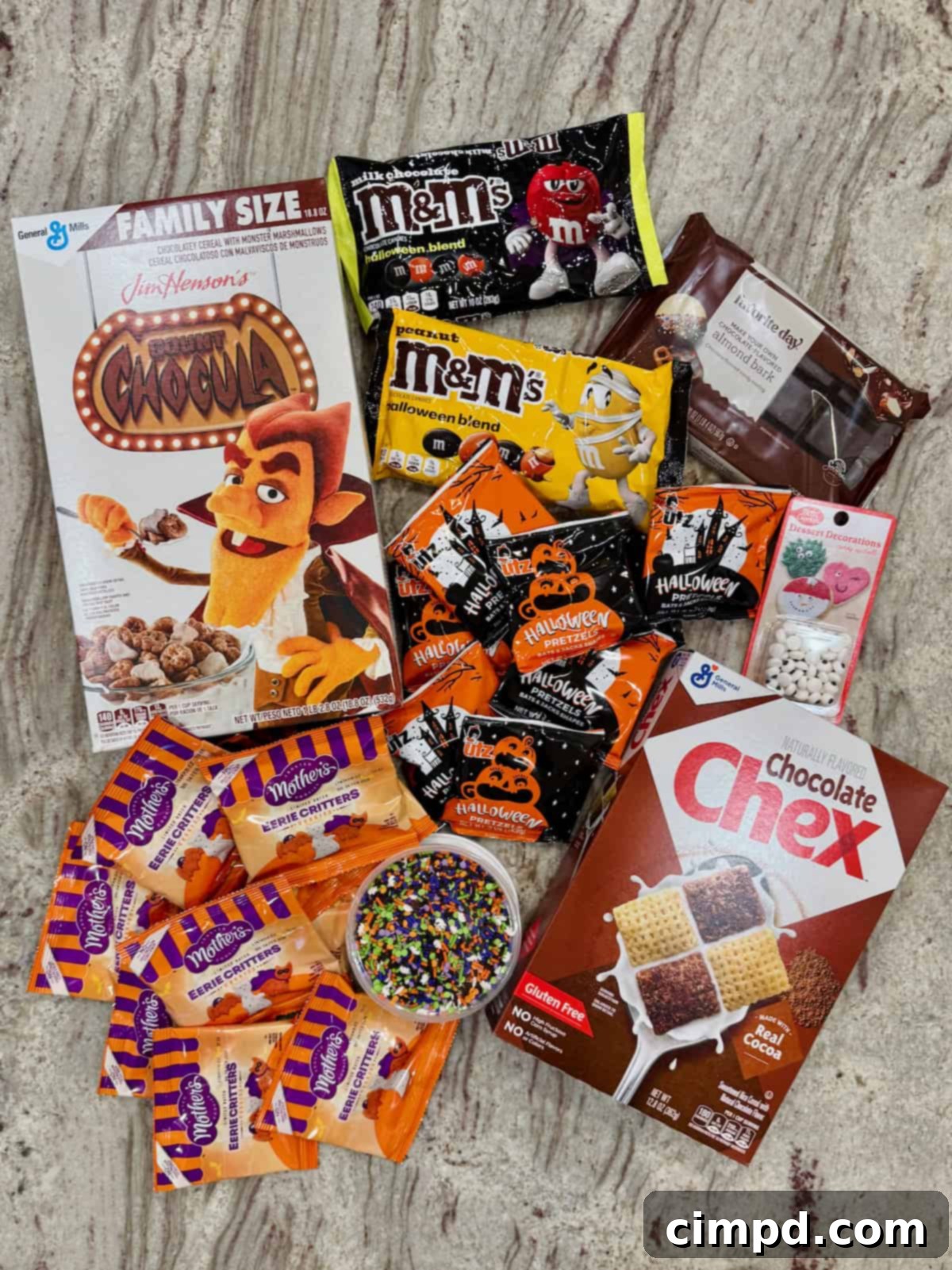 All the vibrant and spooky ingredients laid out neatly on a gray marble counter, ready to be transformed into the ultimate Halloween snack mix.