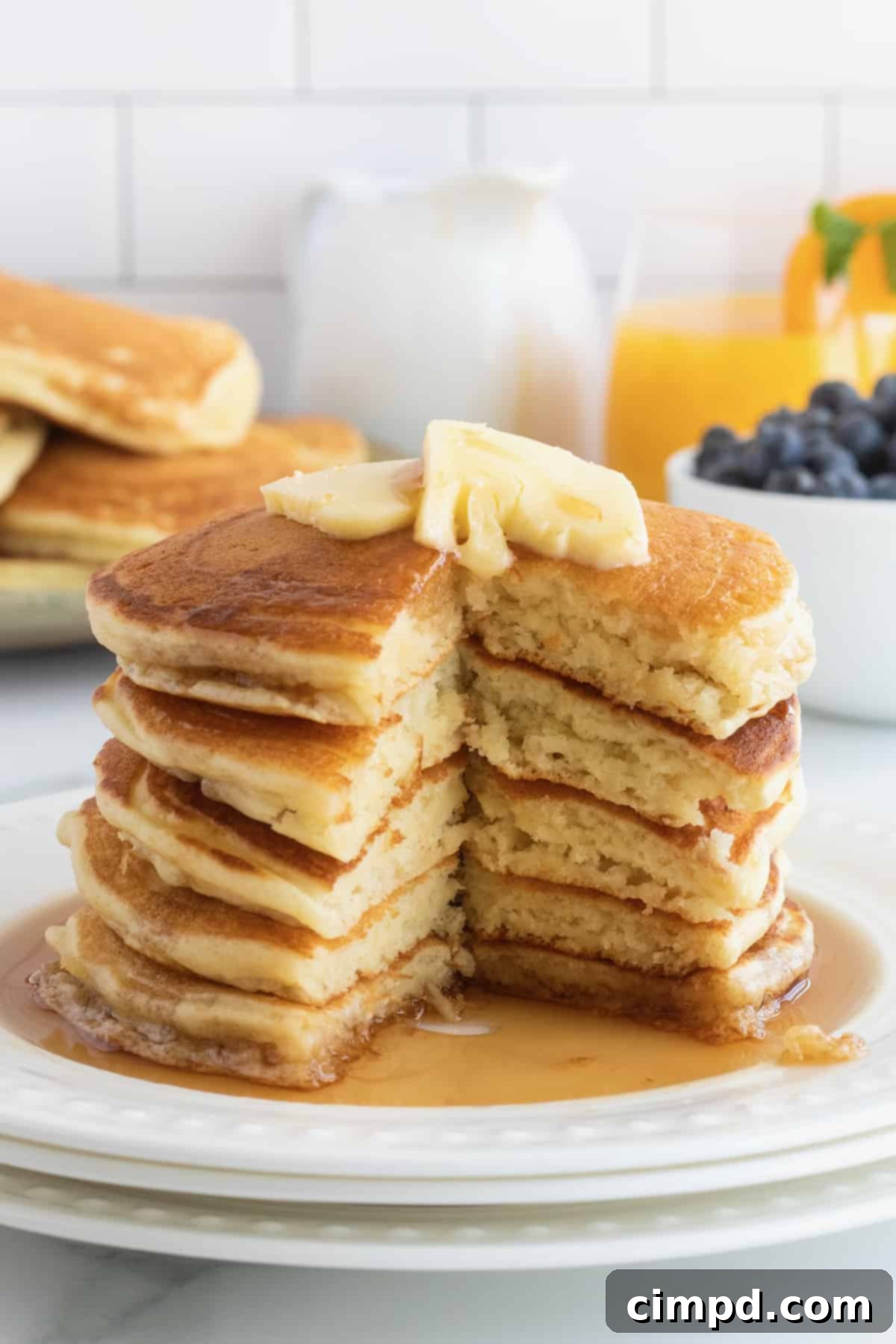 Stack of golden Classic Buttermilk Pancakes drizzled with maple syrup and butter, by The BakerMama