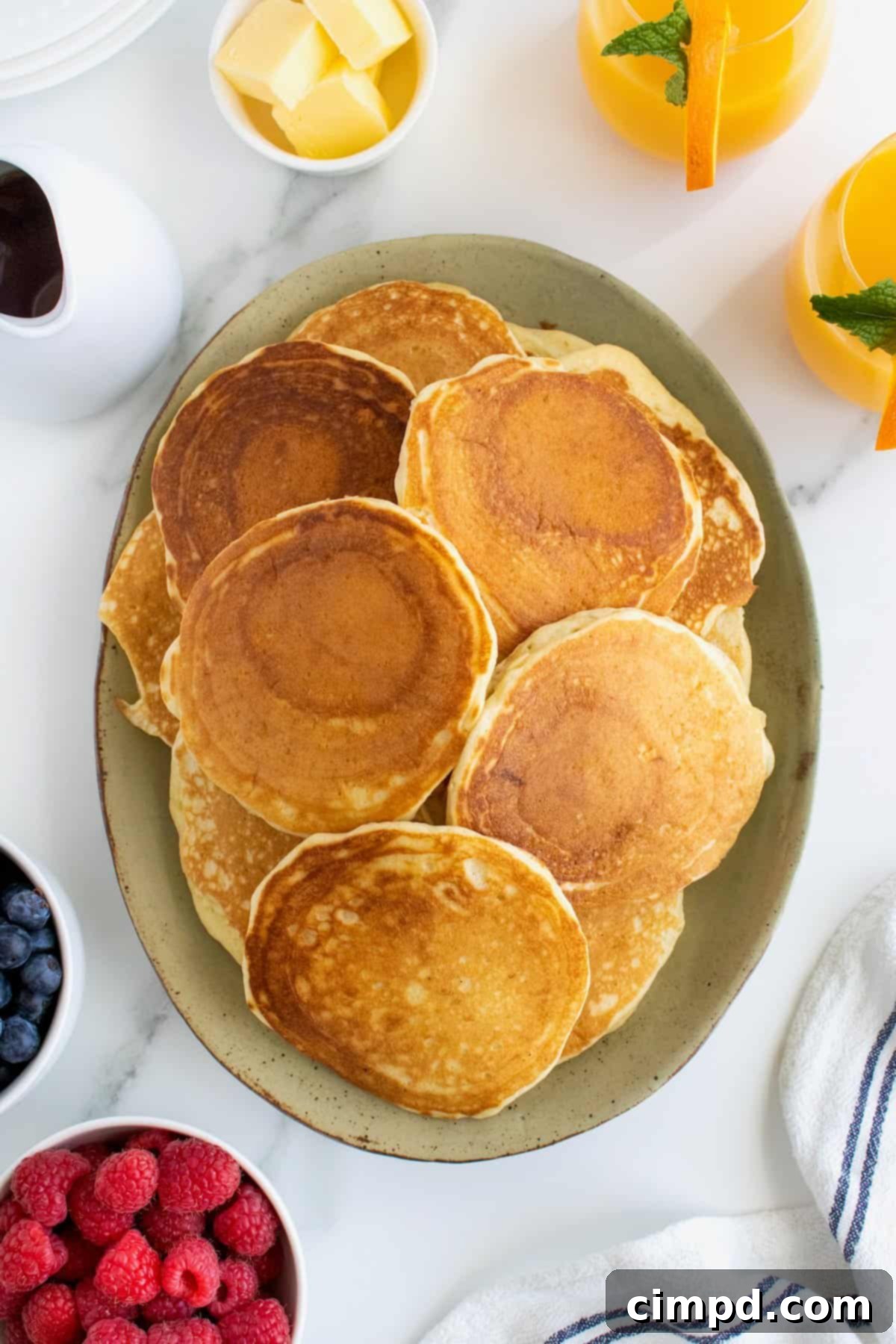 Buttermilk Pancakes with butter, syrup, and a side of fruit and bacon, by The BakerMama
