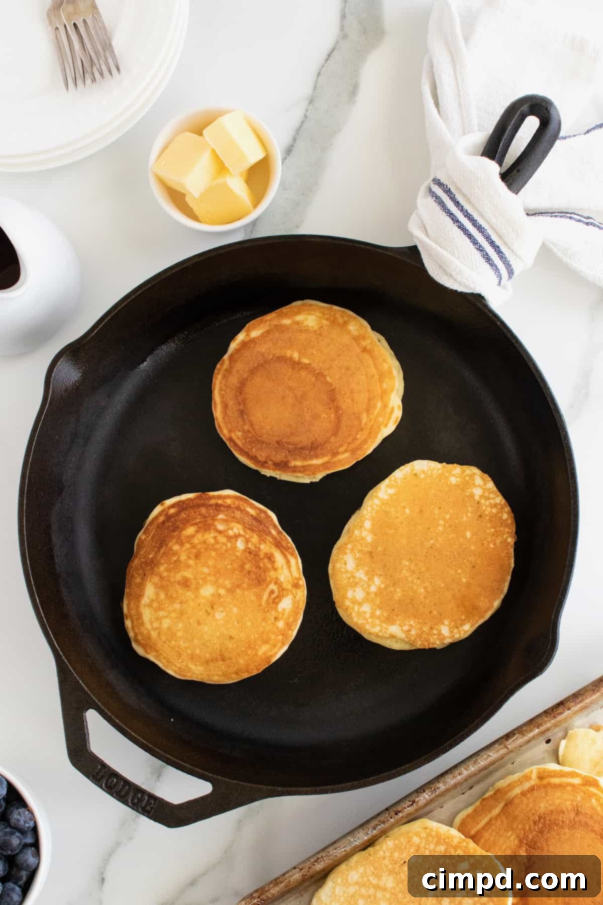 Golden-brown Classic Buttermilk Pancakes cooking on a griddle, ready to be flipped, by The BakerMama