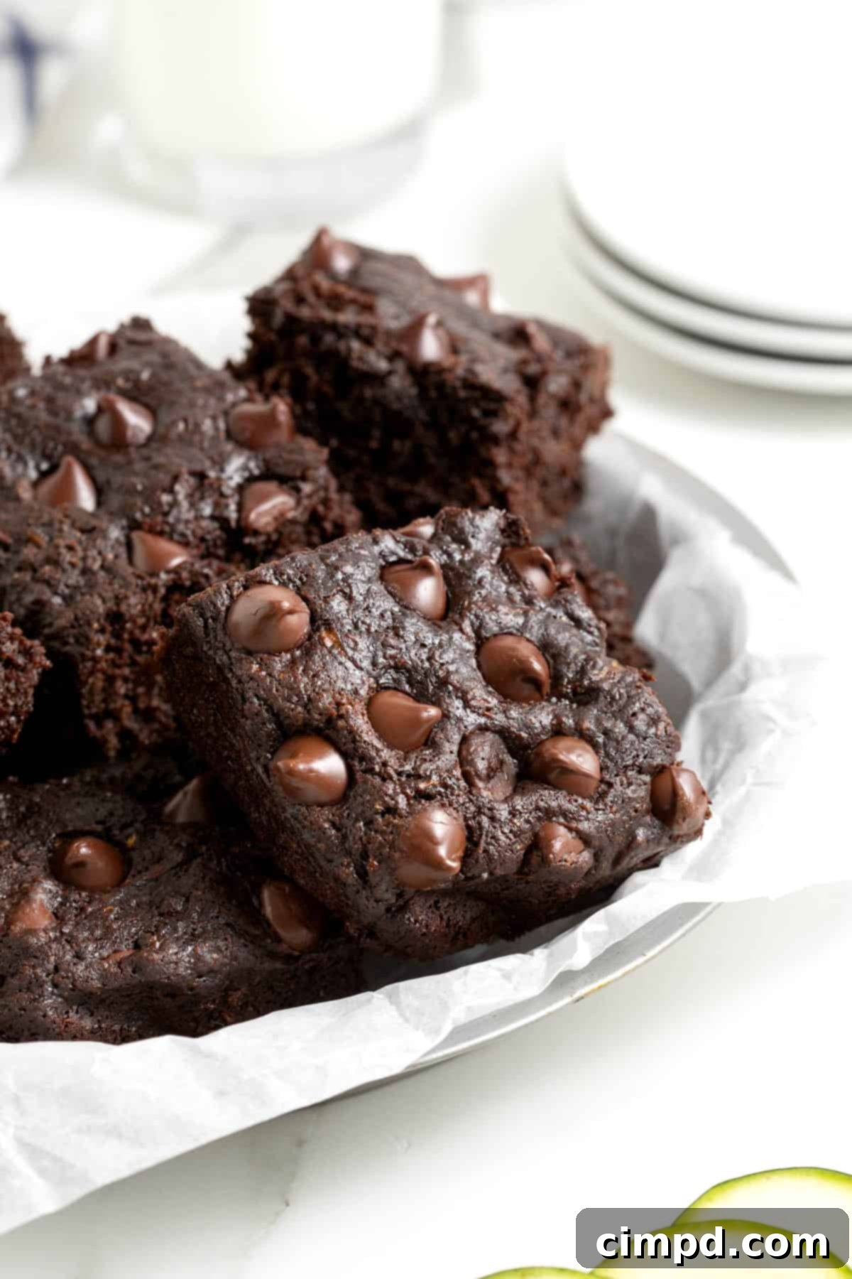A pristine white plate holds a generous pile of dark chocolate zucchini brownies, artfully arranged on a sleek white marble counter, showcasing their rich color and inviting texture.