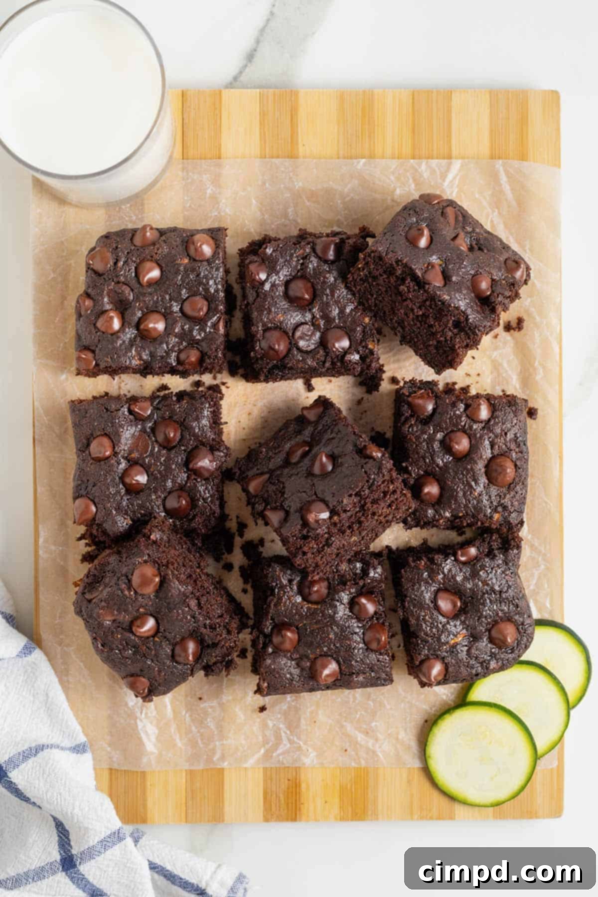 An array of freshly baked dark chocolate zucchini brownies, cooling on a wooden cutting board lined with parchment paper, showcasing their rich, fudgy texture and inviting appearance.