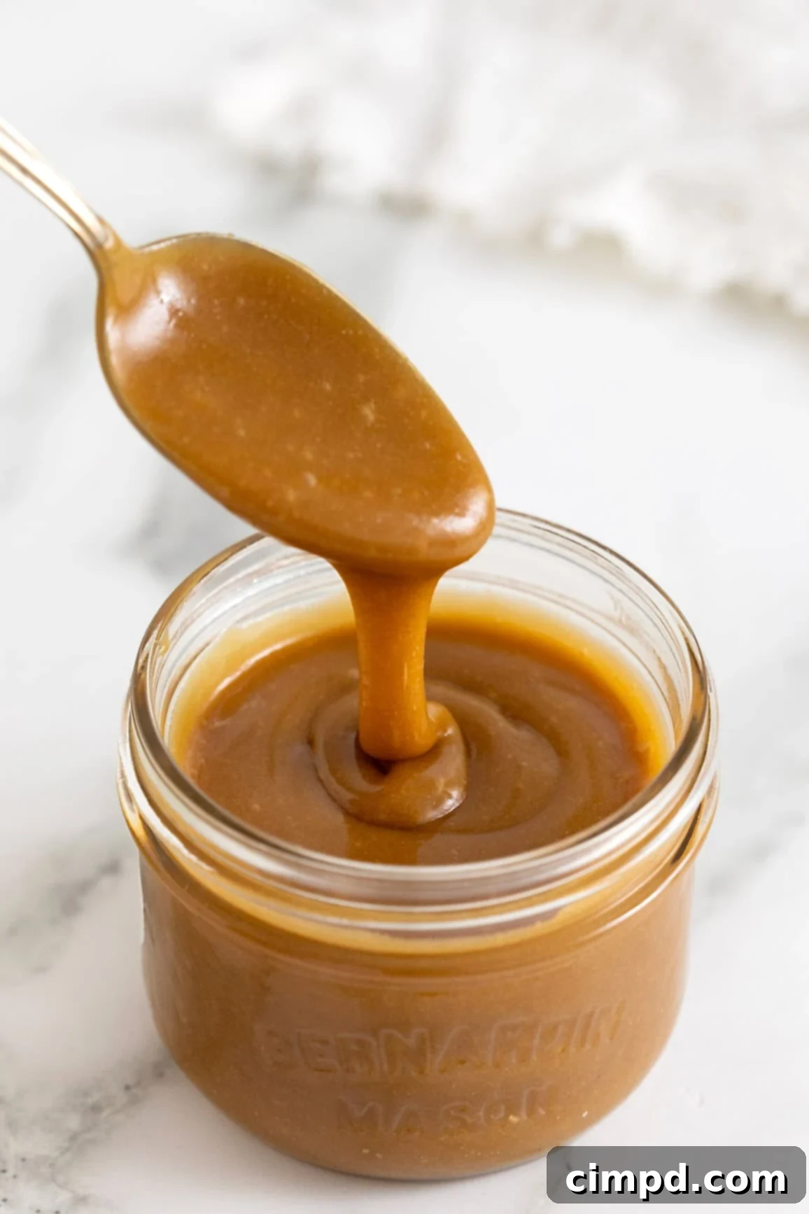 Making Luscious Caramel: A Beginner's Guide 2 A spoonful of creamy caramel sauce being lifted from a mason jar.