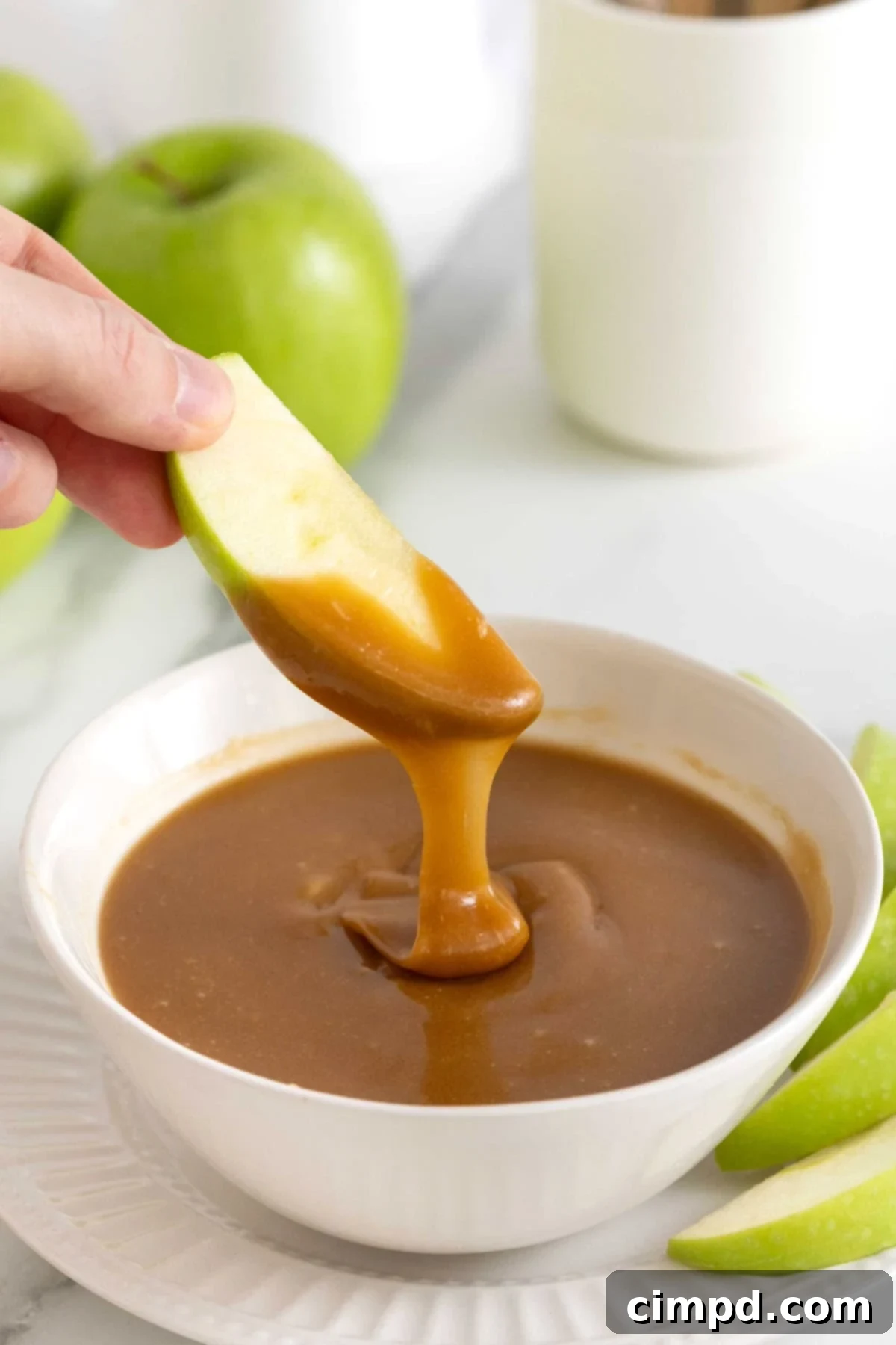 Making Luscious Caramel: A Beginner's Guide 3 A crisp green apple slice being dipped into a bowl of homemade caramel sauce.