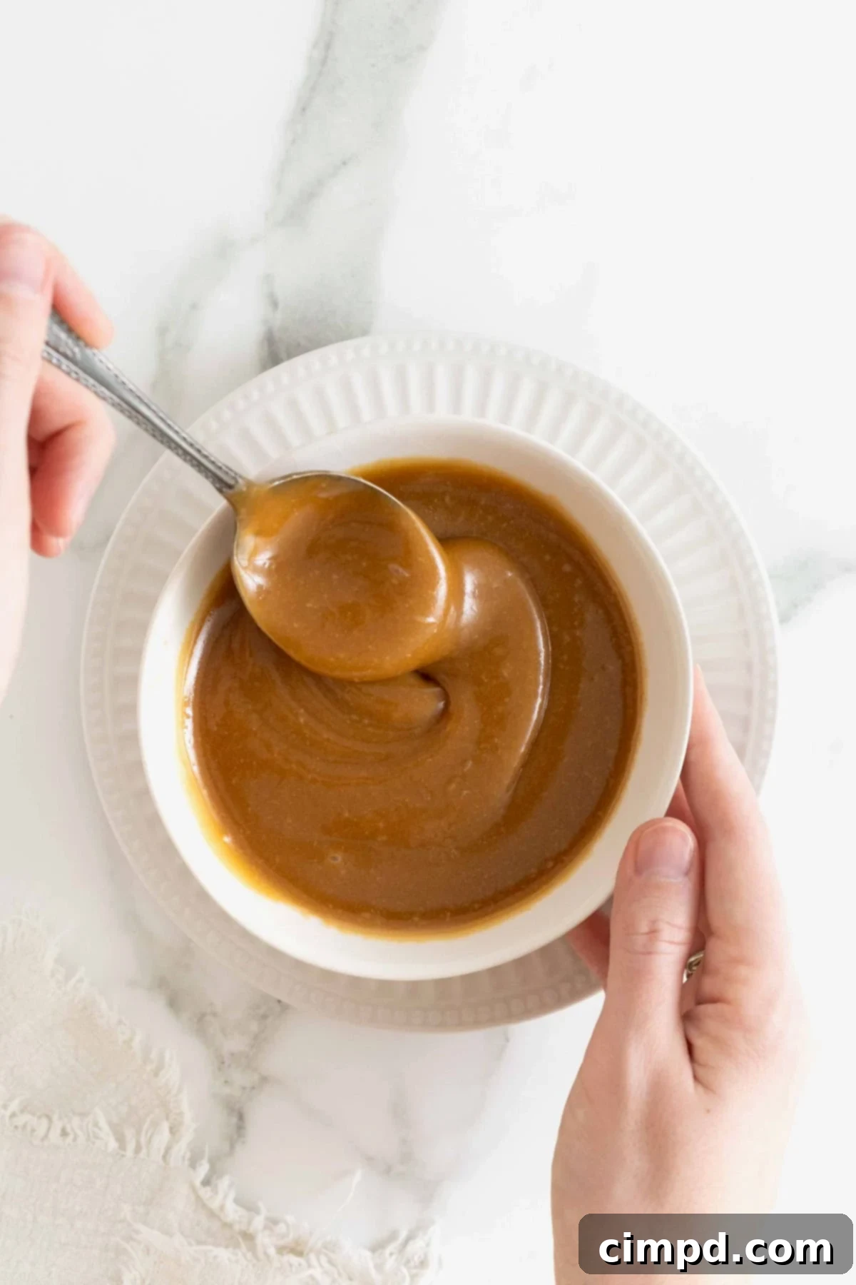 Making Luscious Caramel: A Beginner's Guide 4 A metal spoon stirring smooth caramel sauce in a white bowl.
