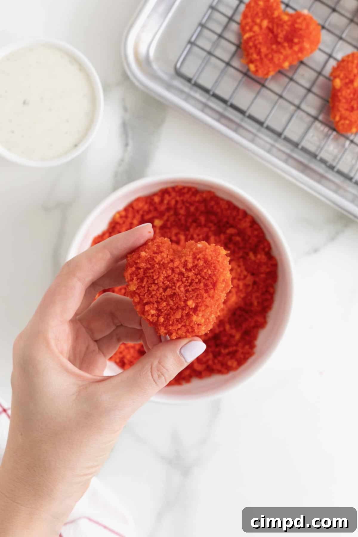 Fiery Cheetos Mozza Hearts 10 A mozzarella heart being dipped into a bowl of Cheeto crumbs.